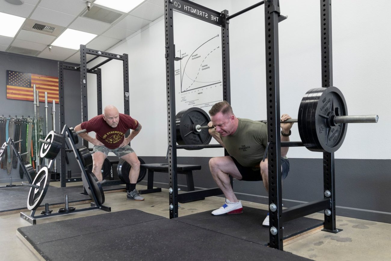 A man squats four plates (405 pounds) while another man watches.