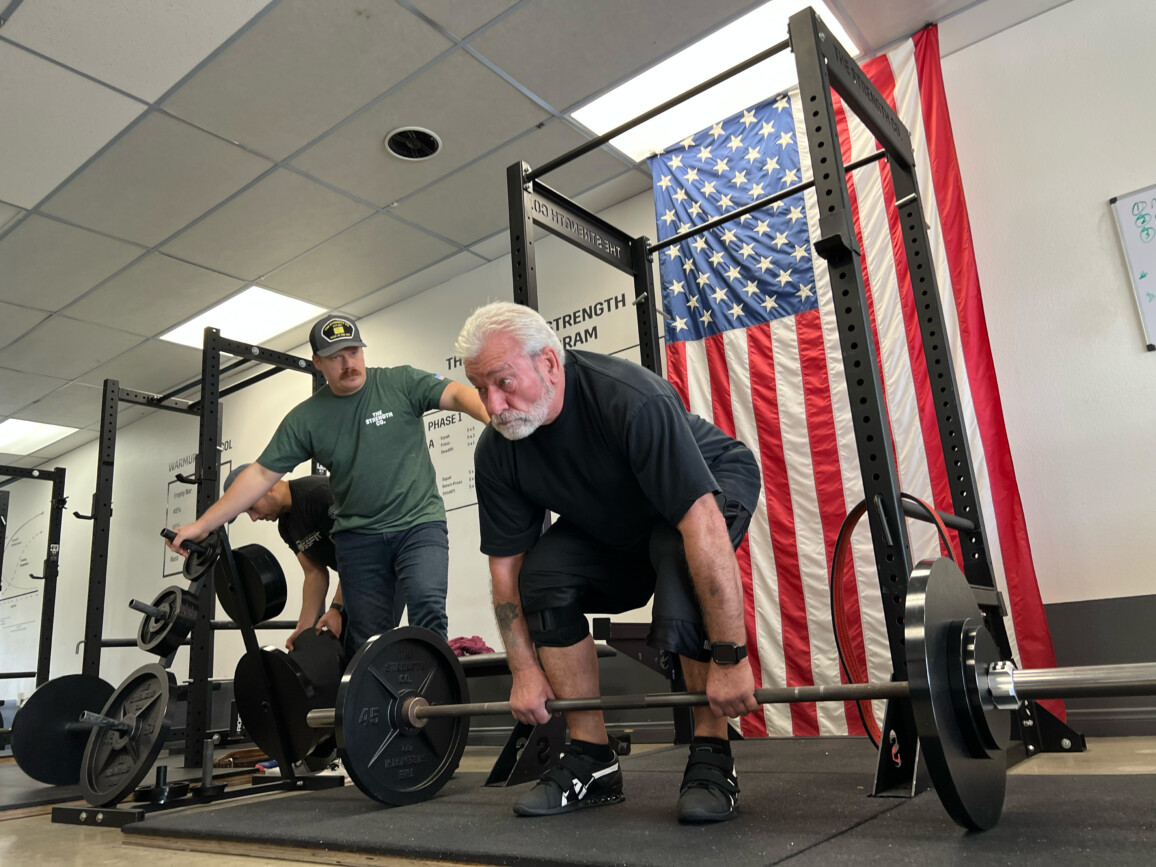 A man with white hair preparing to deadlift a barbell.