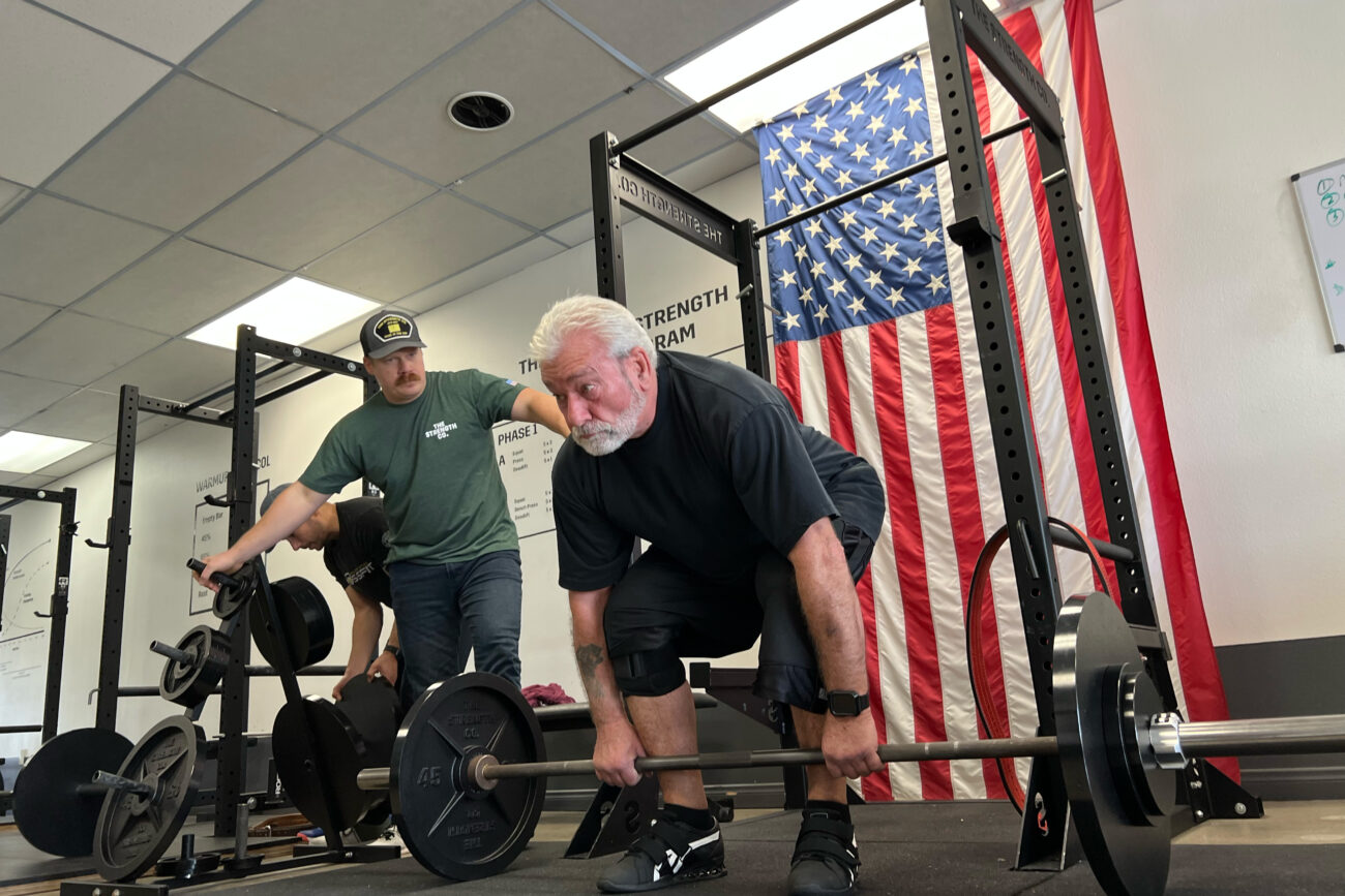 A man with white hair preparing to deadlift a barbell.